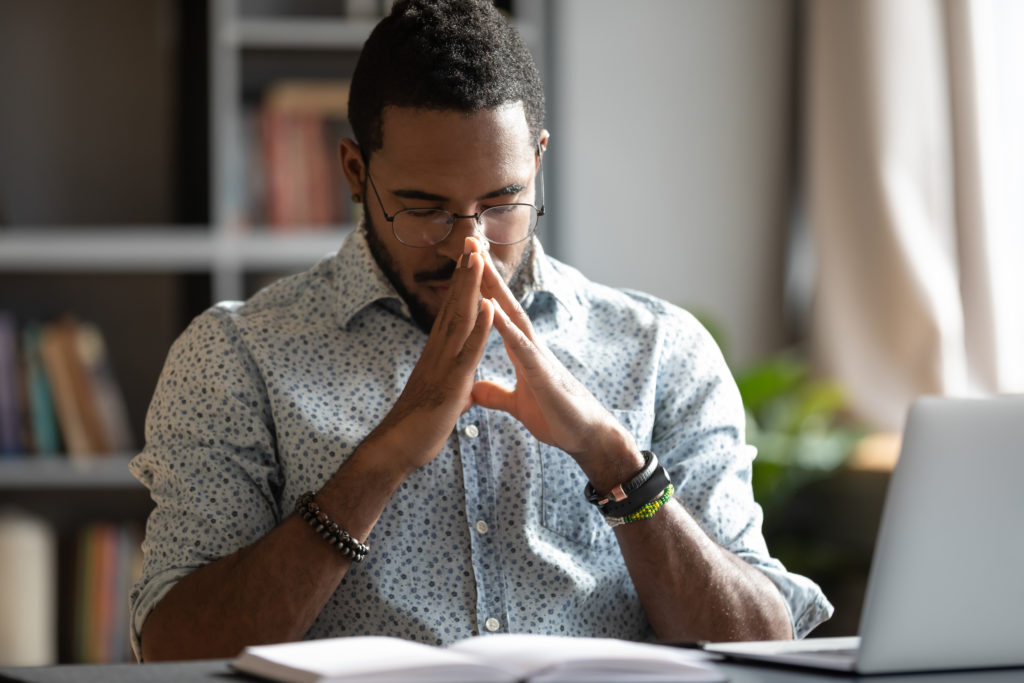 A young Black man prays at his desk as he asks, "Is meditation a sin?"