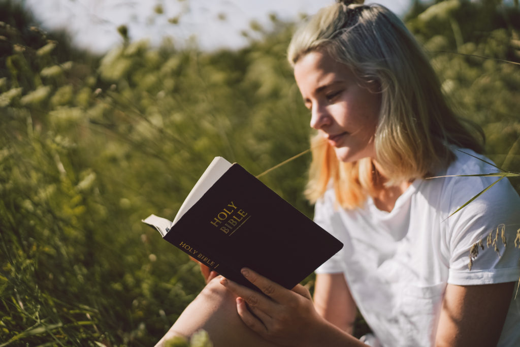 Young woman in white T-shirt holds a Bible outside and asks the question "Is meditation a sin?"